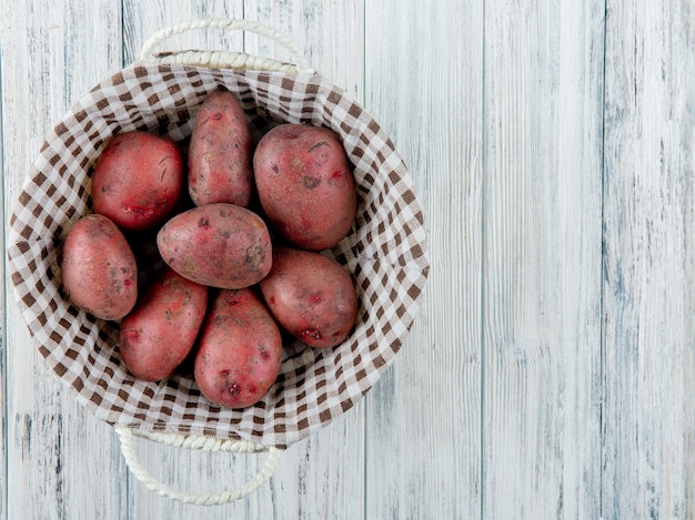 Vista superior da cesta cheia de batatas no lado esquerdo e fundo de madeira com espaço de cópia