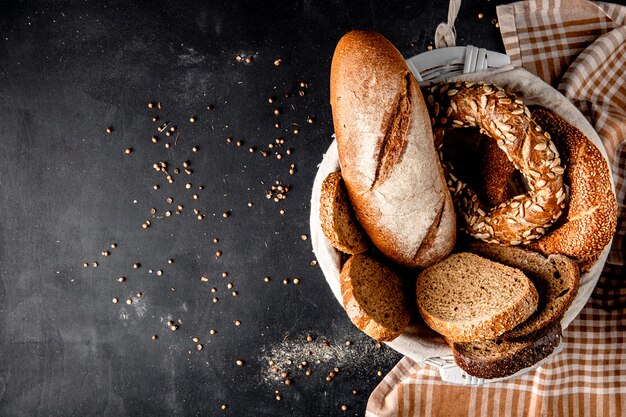 Vista superior da cesta cheia de pães como baguette bagel centeio com sementes de girassol na superfície preta