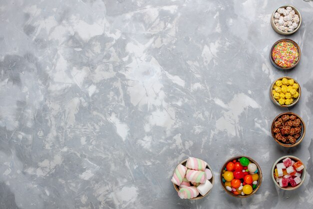 Vista superior da composição de doces, doces de cores diferentes com marshmallow dentro de potes na mesa branca.