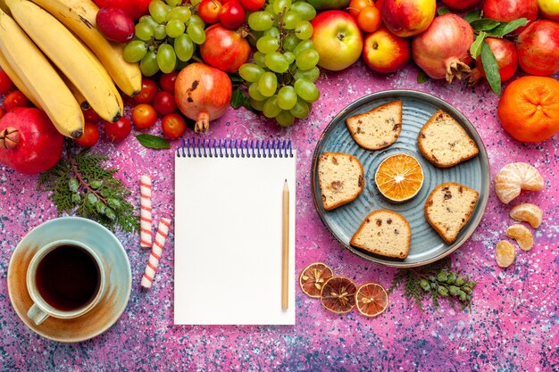 Vista superior da composição de frutas frescas frutas coloridas com bolos fatiados e xícara de chá na mesa rosa