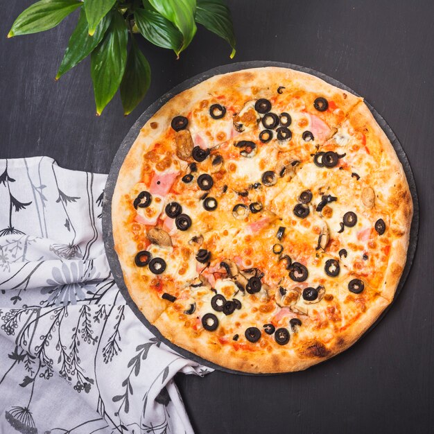 Vista superior da deliciosa pizza em ardósia com plantas e roupas