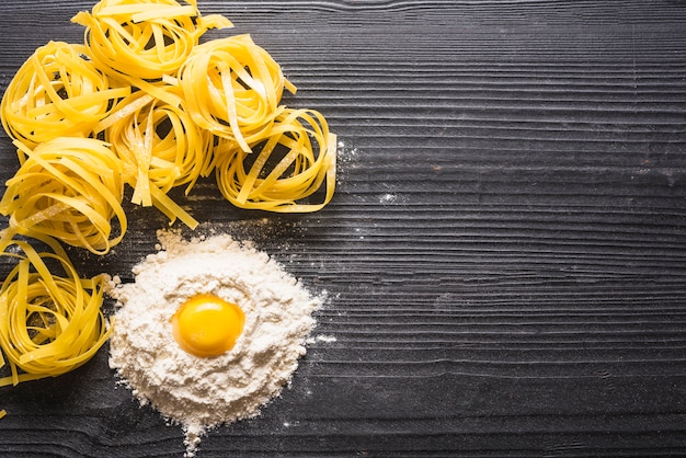 Foto grátis vista superior da gema de ovo com farinha e tagliatelle cru no contexto de madeira