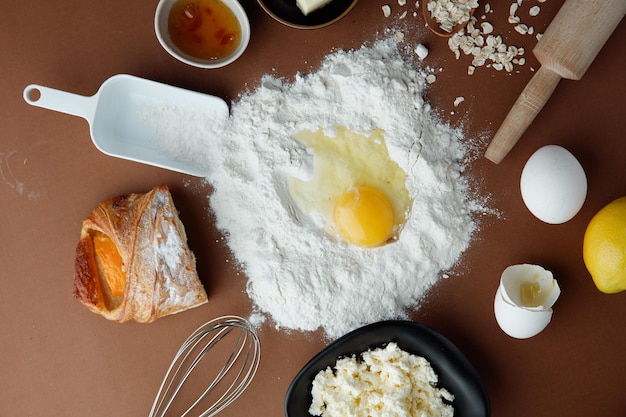 Vista superior da gema de ovo na farinha com croissant de geléia meio queijo cottage limão ovo aveia com colher medida rolo e bata no fundo branco