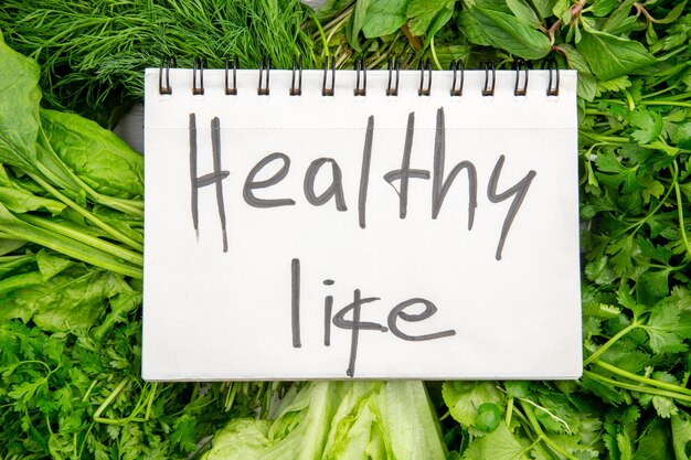 Vista superior da inscrição de vida saudável no caderno espiral em fardos de verduras frescas na mesa branca