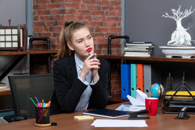 Vista superior da jovem assistente sentada em sua mesa, pensando profundamente no escritório