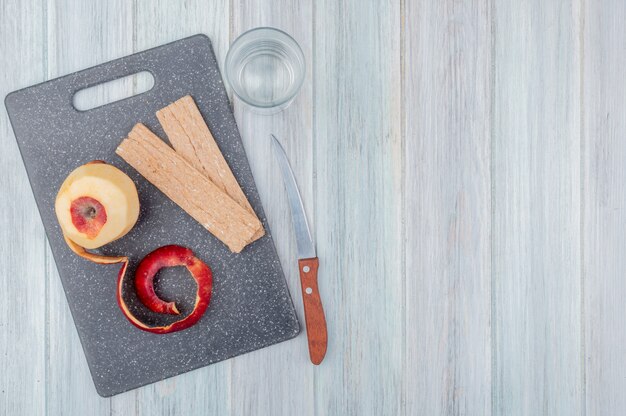 vista superior da maçã vermelha com casca e biscoitos na tábua com faca e copo de água na mesa de madeira com espaço de cópia