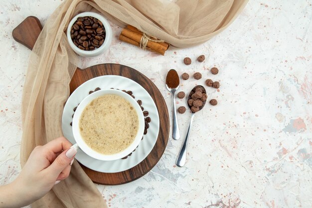 Vista superior da mão segurando uma xícara de café e feijão canela em pó limões toalha de cor nude no fundo branco