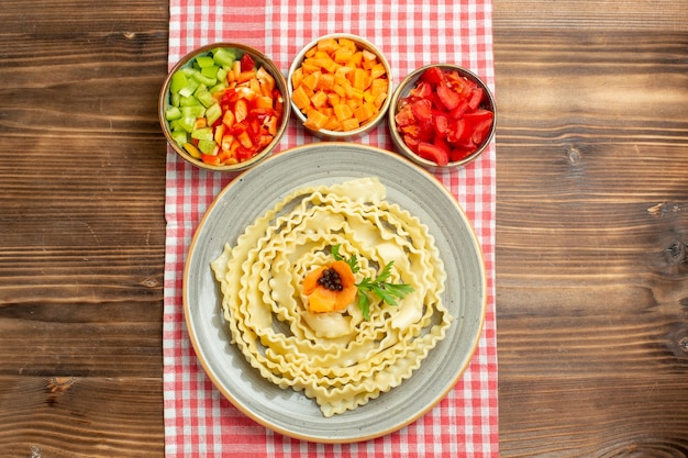 Vista superior da massa crua com vegetais fatiados no produto de ingrediente alimentar de refeição de vegetais de mesa marrom