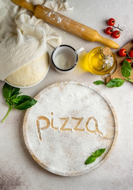 Vista superior da massa de pizza com tomate e palavra escrita em farinha