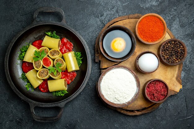 Vista superior da massa italiana crua com verduras de carne e molho de tomate dentro da panela no fundo cinza escuro