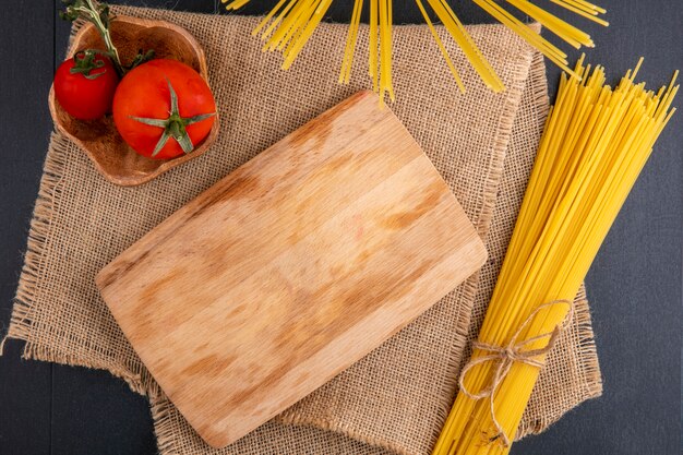 Vista superior da mesa da cozinha com espaguete cru e tomate em um guardanapo bege em uma superfície preta