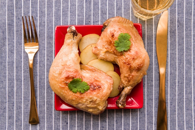 Foto grátis vista superior da perna de frango assado gourmet no prato com garfo e faca de manteiga na toalha de mesa