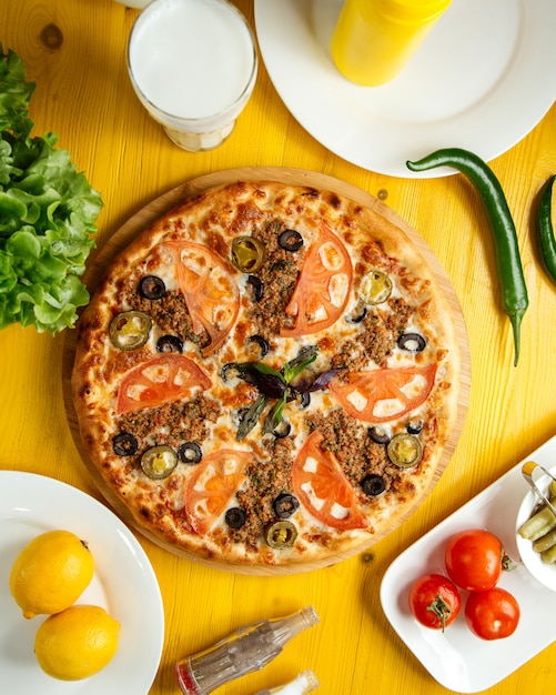 Vista superior da pizza com carne picada, tomate e azeitonas em uma placa de madeira