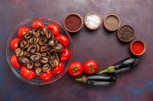 Vista superior da refeição de vegetais fatiados e enrolados com tomates com berinjela e temperos na mesa escura