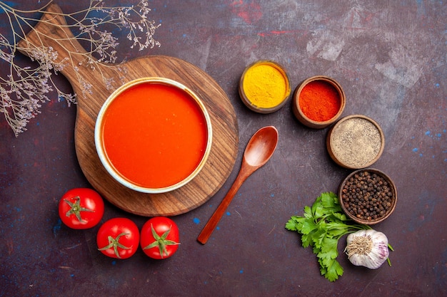 Vista superior da saborosa sopa de tomate com tomates frescos e temperos no escuro