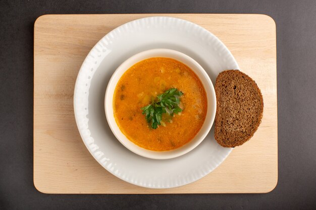 Vista superior da saborosa sopa de vegetais dentro do prato com pão de forma na superfície escura