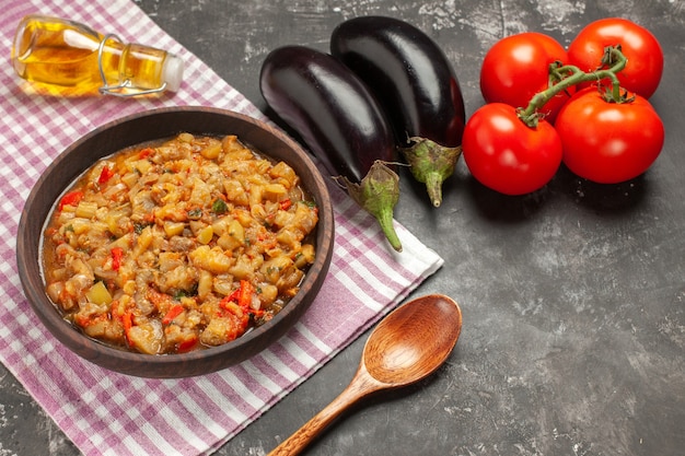 Foto grátis vista superior da salada de berinjela assada em uma tigela colher de pau tomate berinjela garrafa de óleo na superfície escura