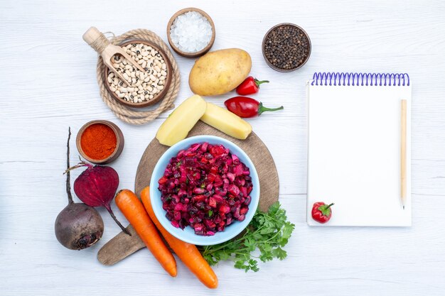 Vista superior da salada de beterraba fresca com vegetais fatiados, juntamente com o bloco de notas de batata, cenoura, feijão cru, mesa de luz, salada de vegetais fresca de refeição alimentar