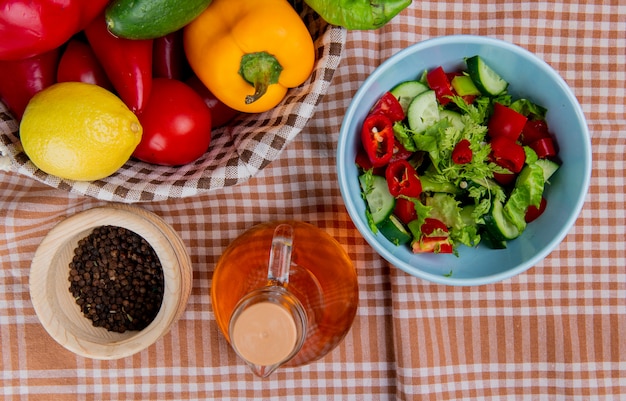 Vista superior da salada de legumes com pepino limão tomate pimenta na cesta com sementes de pimenta preta e manteiga derretida no pano xadrez