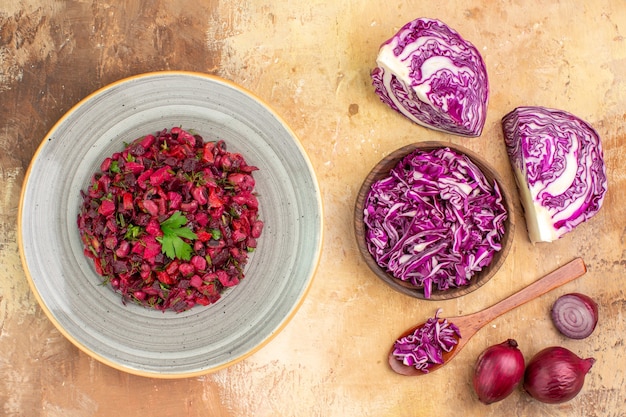 Foto grátis vista superior da salada de legumes fresca em um prato de cerâmica feito de uma tigela de repolho roxo picado e cebola roxa em um fundo de madeira