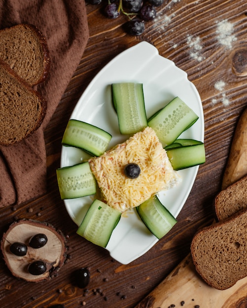 Foto grátis vista superior da salada de mimosa em porções em prato branco, guarnecido com fatias de pepino