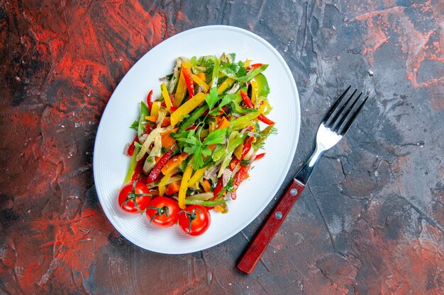 Vista superior da salada de vegetais em um garfo oval em uma mesa vermelha escura