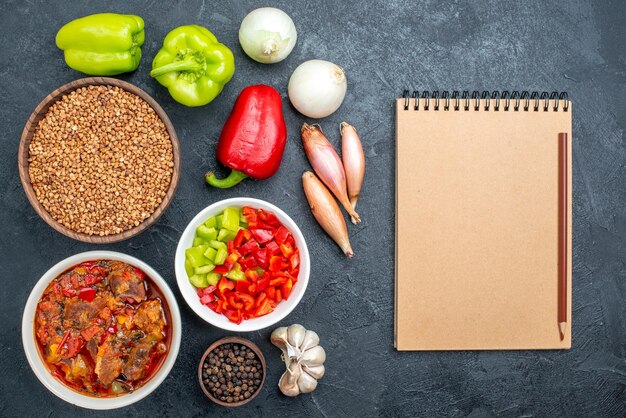 Vista superior da sopa de carne com vegetais e trigo sarraceno cru no espaço escuro