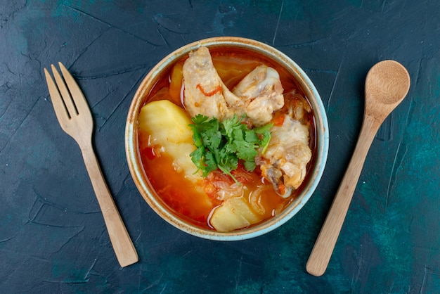 Foto grátis vista superior da sopa de galinha com frango e verduras dentro, juntamente com talheres de madeira na mesa azul-escura sopa carne comida jantar frango