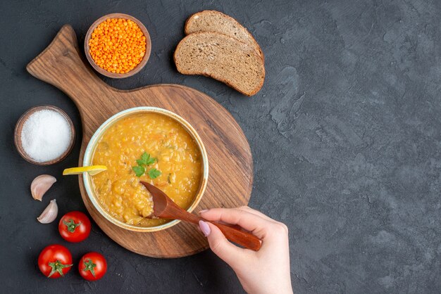 Vista superior da sopa de lentilha com tomate salgado e pães escuros na superfície escura