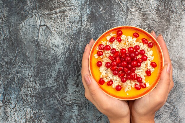 Vista superior da tigela de frutas vermelhas com sementes de romã de aveia nas mãos