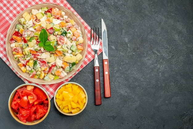 Foto grátis vista superior da tigela de salada de legumes no guardanapo vermelho com vegetais e talheres ao lado e com espaço livre para texto na mesa escura