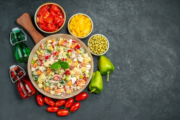 Vista superior da tigela de salada de vegetais no suporte do prato com vegetais e garrafas de óleo e vinagre ao lado e coloque para o seu texto em fundo cinza escuro