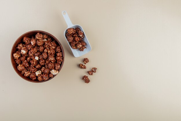 Vista superior da tigela e colherada de pipoca de chocolate no lado esquerdo e superfície branca com espaço de cópia