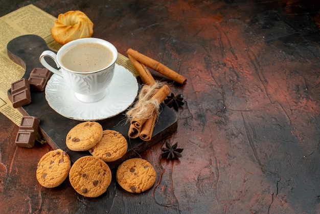 Vista superior da xícara de café na tábua de madeira, biscoitos, lima e canela, barras de chocolate no lado direito na superfície escura
