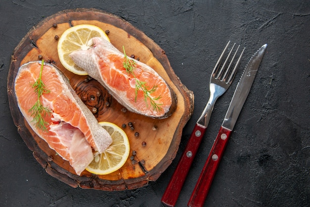 Vista superior das fatias de peixe fresco com limão e talheres na mesa escura