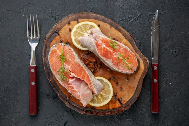 Vista superior das fatias de peixe fresco com limão e talheres na mesa escura