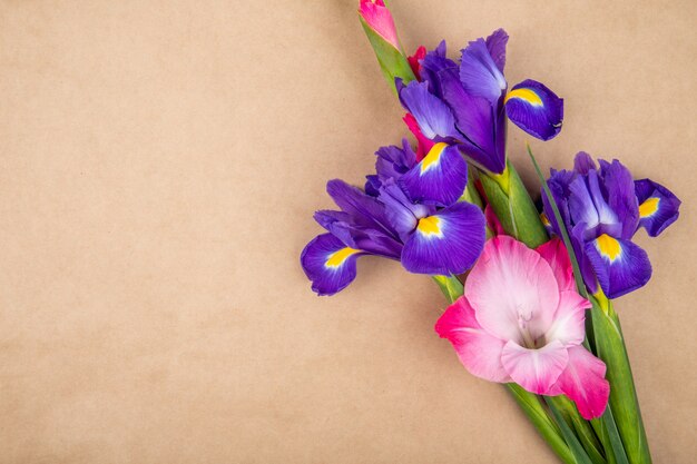 Vista superior das flores de íris e gladíolo de cor roxa e rosa escura, isoladas no fundo de textura de papel marrom com espaço de cópia