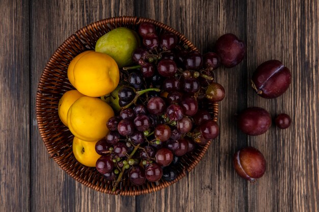 Vista superior das frutas como nectacotes de pluot de uva em uma cesta e pluots king de sabor em fundo de madeira