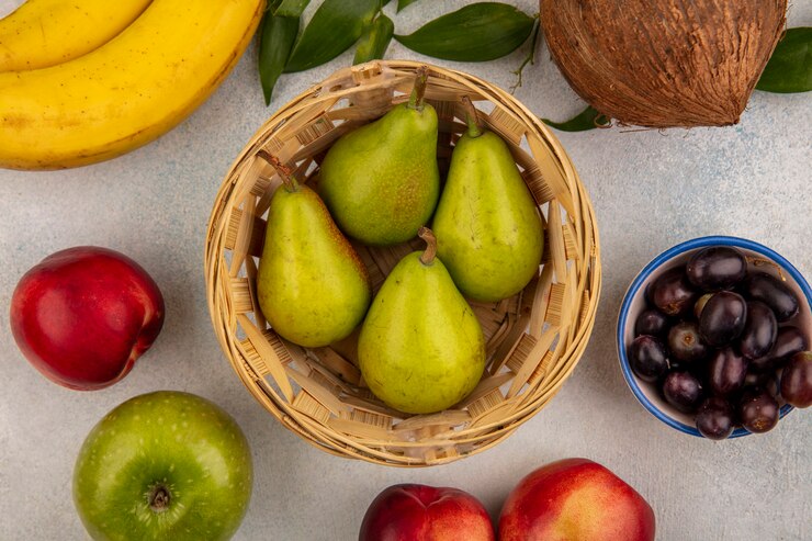 Foto grátis vista superior das frutas como tigela de pêra com maçã, pêssego, banana, coco, bagas de uva com folhas no fundo branco