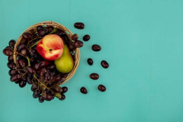 Vista superior das frutas como uma cesta de uva e pêssego com bagas de uva no fundo azul com espaço de cópia