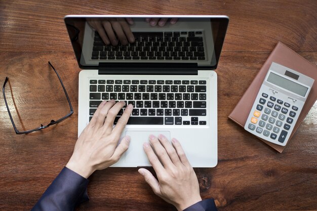 Vista superior das mãos do homem de negócios trabalhando no laptop ou tablet pc na mesa de madeira.