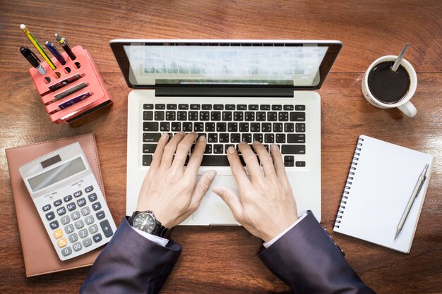 Vista superior das mãos do homem de negócios trabalhando no laptop ou tablet pc na mesa de madeira.