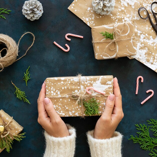 Vista superior das mãos segurando um presente de Natal com papel de embrulho pintado