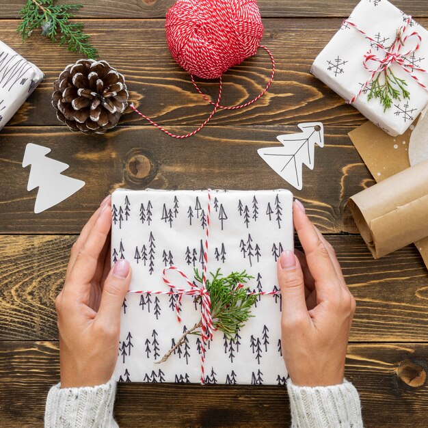 Vista superior das mãos segurando um presente de Natal com pinha e cordão