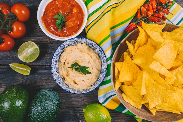 Vista superior das microplaquetas mexicanas dos nachos; abacate; molho de salsa; tomate cereja; Pimentões vermelhos e limão na mesa