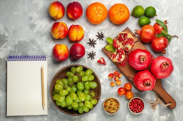 Vista superior das romãs vermelhas frescas, frutas azedas e maduras com uvas verdes frescas na mesa branca