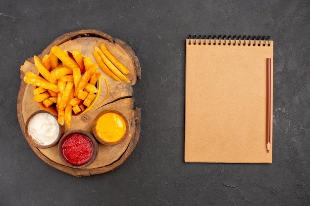 Foto grátis vista superior das saborosas batatas fritas com molhos no preto