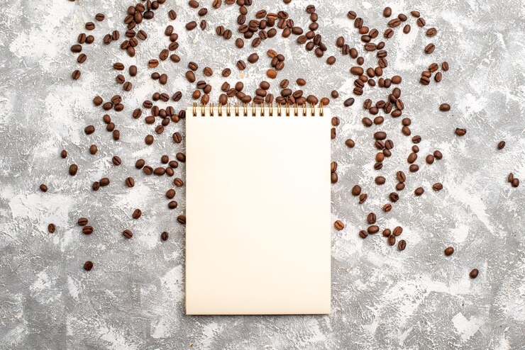 Foto grátis vista superior das sementes de café marrom com o bloco de notas na superfície branca