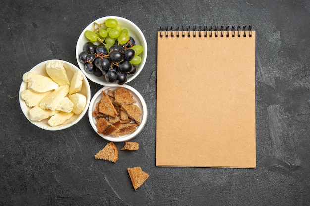 Vista superior das uvas frescas com queijo branco e pão escuro fatiado na superfície escura refeição prato café da manhã frutas com leite