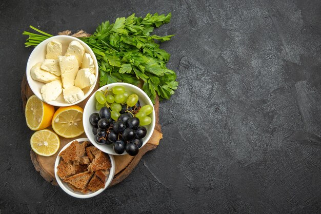 Vista superior das uvas frescas com queijo branco e rodelas de limão na superfície escura.